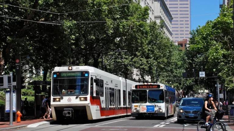 A cyclist riding past a TriMet MAX light rail train and bus stopped at the corner of 5th Ave. and Yamhill St. in Portland, Oregon