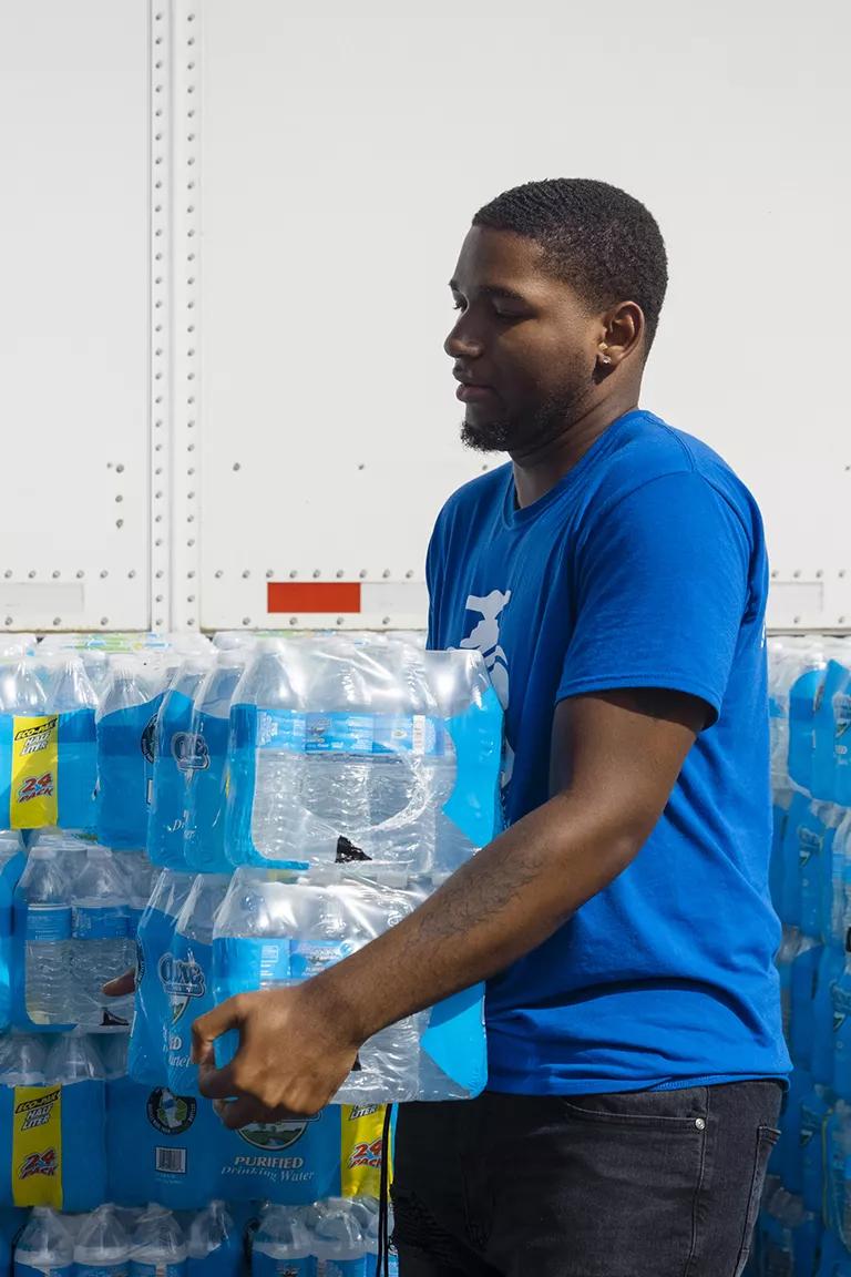 A person in a blue shirt carries packs of bottled water in Benton Harbor, Michigan
