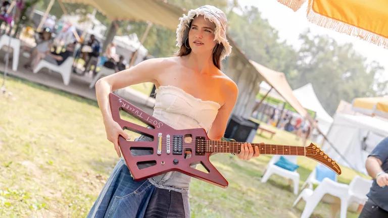 A woman in a hat standing with a guitar at Bonnaroo 2023