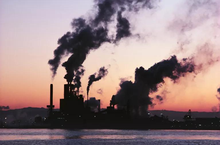 Smoke escaping from industrial smokestacks, with a dusky sky in the background