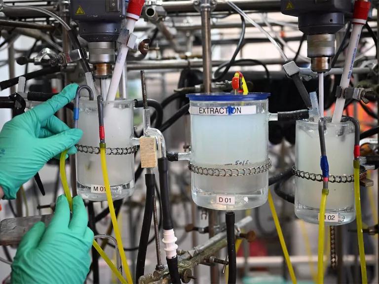 A technician handling beakers filled with chemicals extracted from recycled electric car batteries