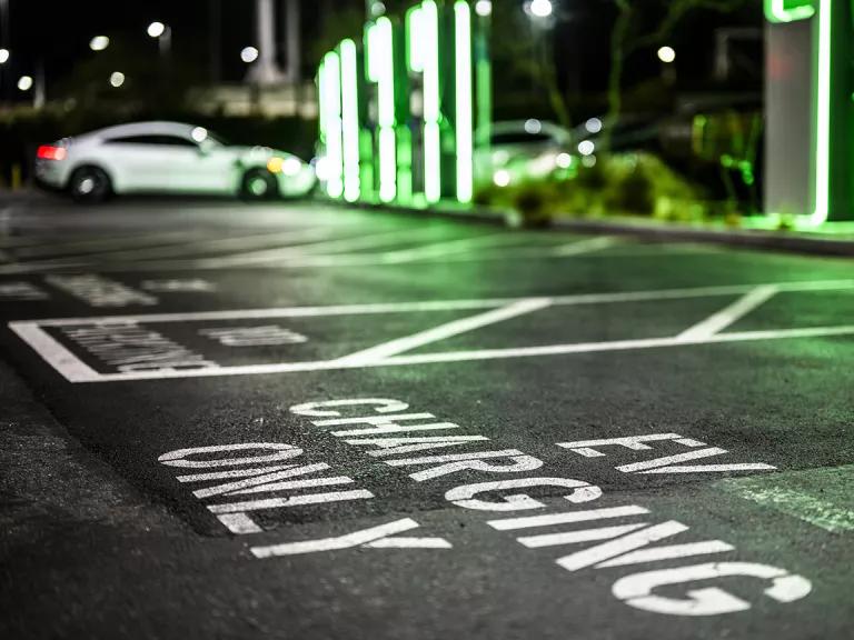 A sign on the ground of a parking lot spot that reads "EV CHARGING ONLY"