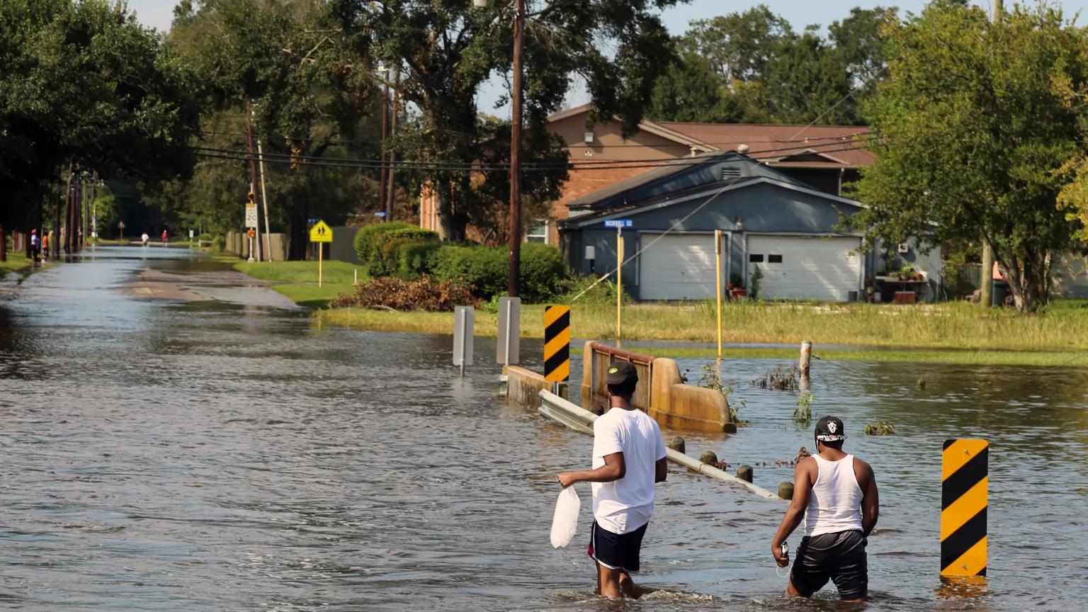 Two people wading through a flooded street in a residential area