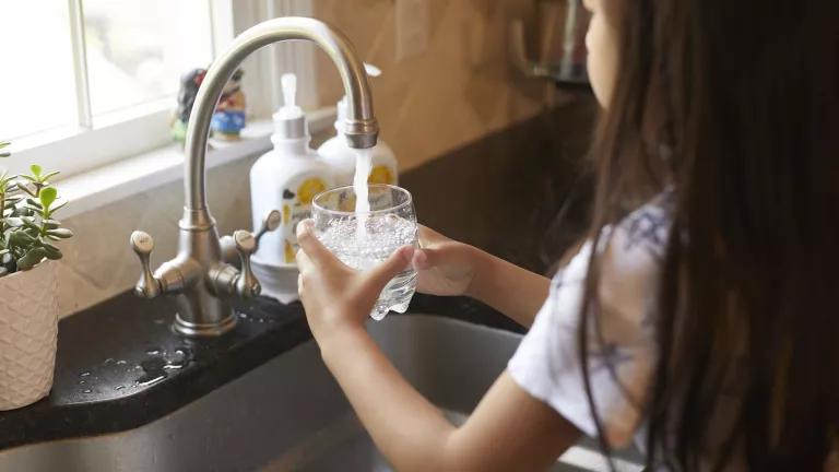 A young girl filling a glass of water in the kitchen sink at her home.