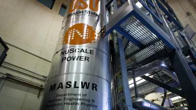 A large metal cylinder with a "NuScale Power" logo stands inside a multi-story room