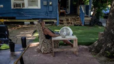 Woman sitting outside a house with a large fan