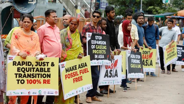 A row of activists hold protest signs in support of renewable energy and against liquefied natural gas in Bangladesh.
