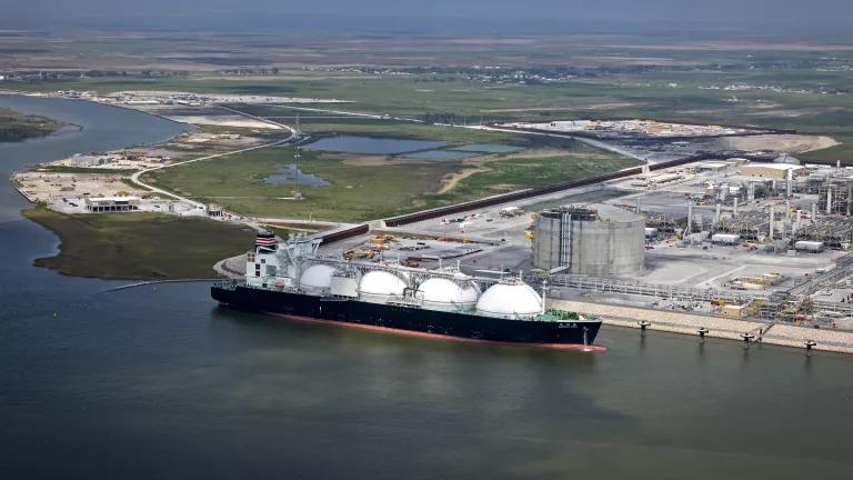 A wide-angle aerial view of a liquefied natural gas tanker ship docked at an export facility in Louisiana