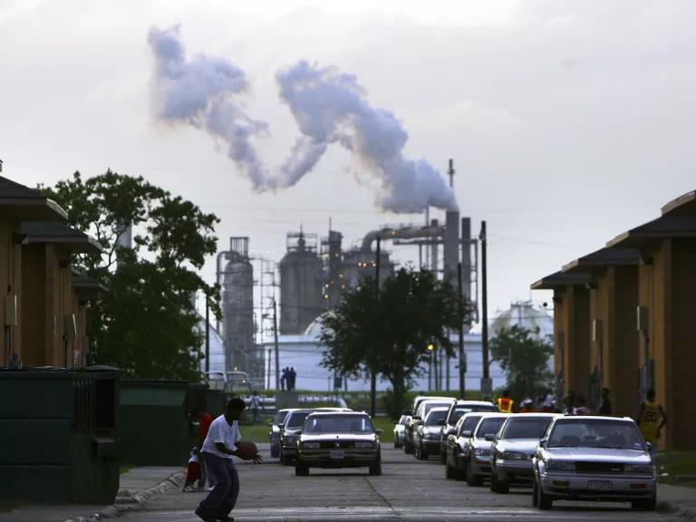 The Carver Terrace housing project is shown next to a smoke-spewing oil refinery in west Port Arthur, Texas, with a person in a white shirt playing basketball on the street