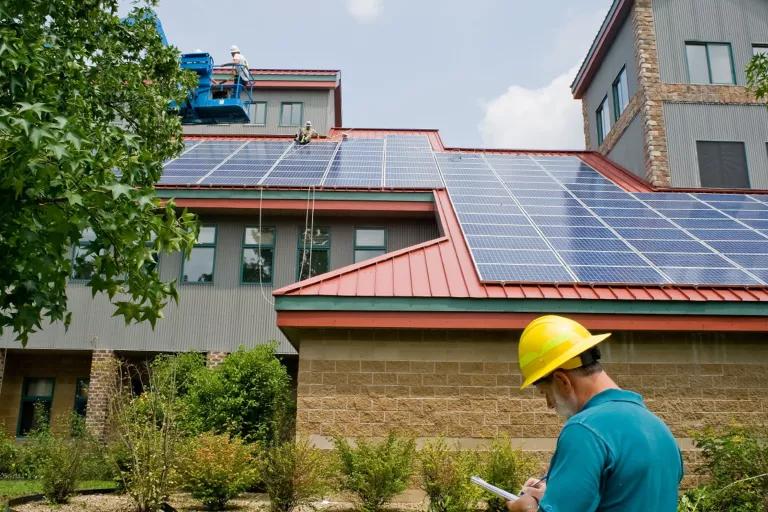 A worker in a hard hat stands in front of a building with rooftop solar panels.