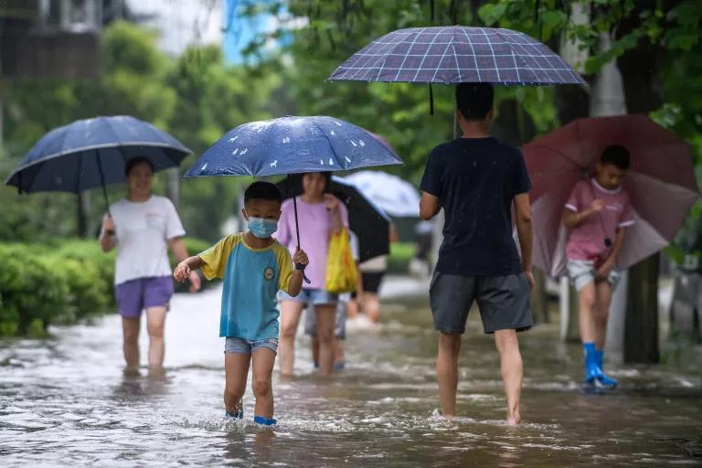 People with umbrellas walk on a street through ankle-deep water