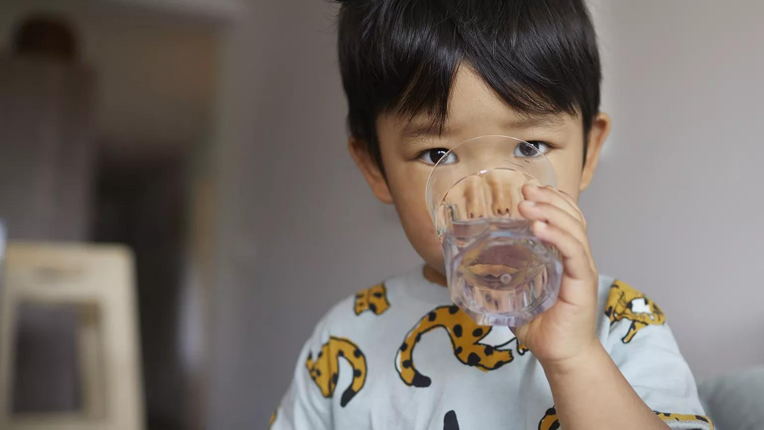 A young child facing the camera and drinking water from a glass