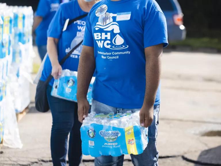 Two people with blue T-shirts carrying bottled water at a pickup site in Benton Harbor, Michigan