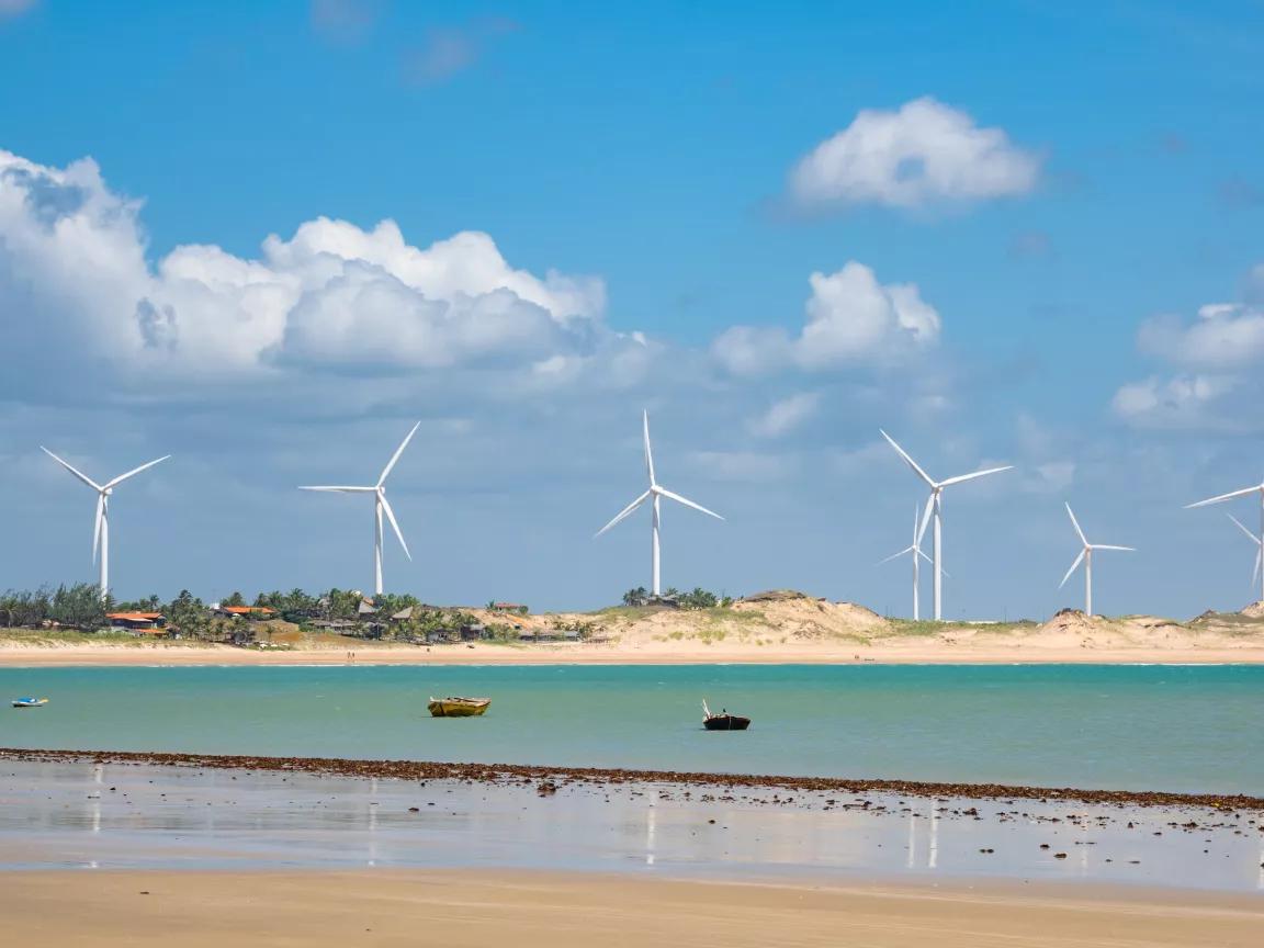 A view of the beach with fishing boats moored and wind turbines in the distance at Icaraí Wind Farm in Ceará, Brazil