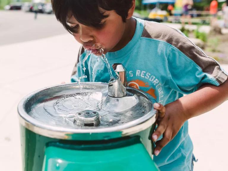 A young boy drinking from an outdoor water fountain.