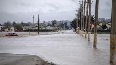A car sinks as floodwaters flow across a road in a residential neighborhood in Monterey County, California.