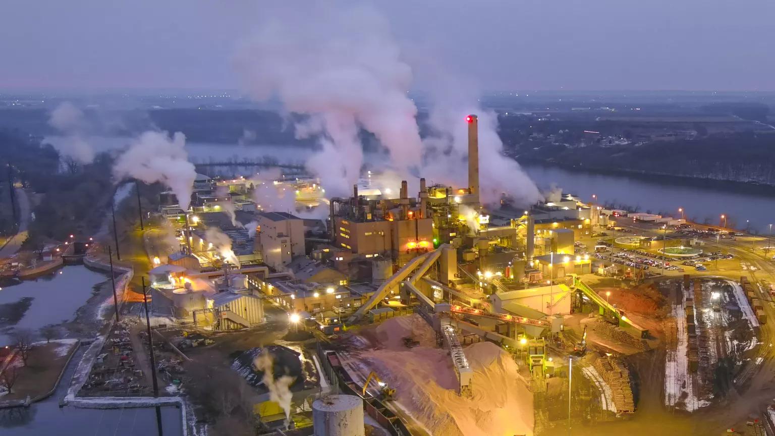 An aerial view of an industrial paper mill spewing out smoke from its buildings into the evening sky in Green Bay, Wisconsin