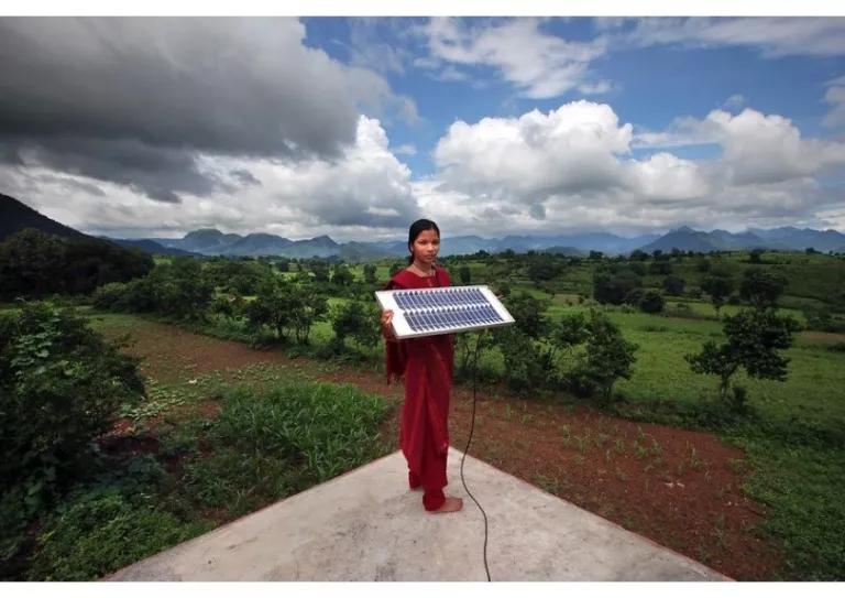 Photo of a girl in India standing against a nature backdrop holding a solar panel