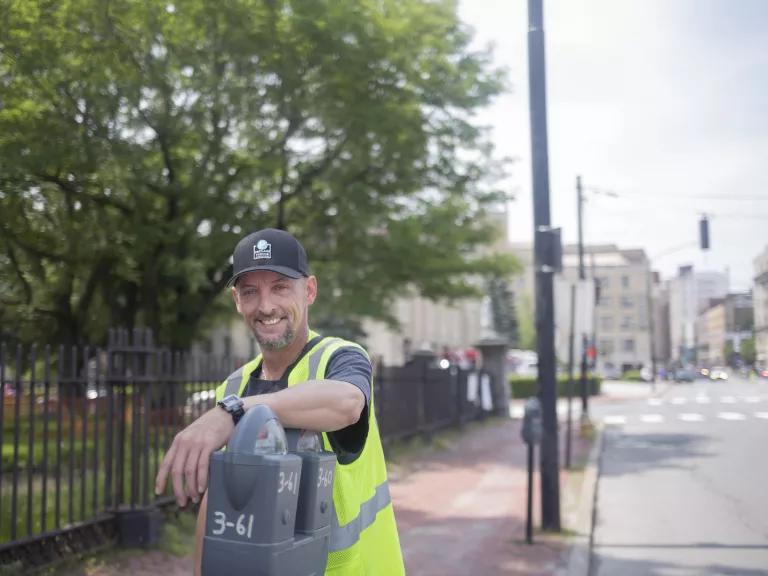 A picture of a man named Tom Jarvis, a parking employee in Portland, Oregon, leaning on a parking meter