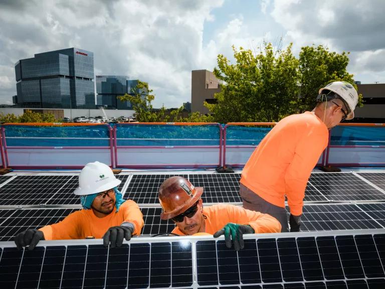 Three Cherry Street Energy workers in bright orange shirts installing rooftop solar panels at the Palisades Office Park in Atlanta